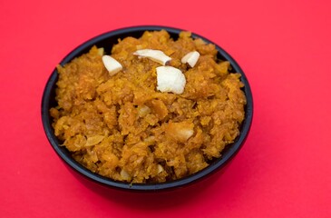 Closeup of Gajar Halwa or Carrot Halva Garnished with Almond and Cashew Nut Cuts in a Black Bowl Isolated on Red Background