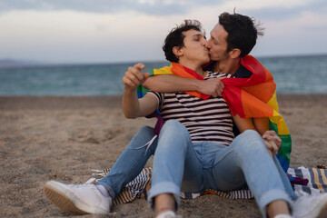 Beautiful gay young couple embraces and holds a rainbow flag. Happy couple enjoy at the beach...
