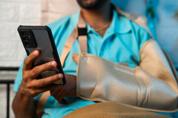 Close up shot of man using mobile phone from broken hand at home - concept of social media addiction, relaxation and treatment.