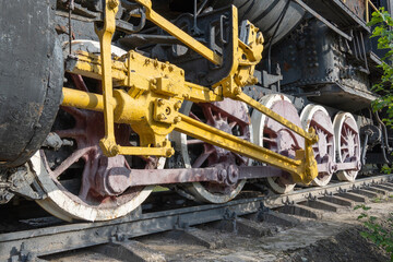Fototapeta premium Close-up drive wheels and rods on steam engine locomotive. Vintage part of suspension of old train. Detailes rarity railway transport - lever and chassis, axle and connection. Parts rail.