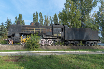 Fototapeta na wymiar Monument old soviet locomotive. Rarity transport of communism. Steam engine train from second world war stands on pedestal in city park. Inscription says - USSR and forward on west. Dnipro Ukraine.