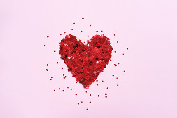 Valentine's day background. Heart made of shiny red small decorative hearts on a pink background strewn with sparkles. Flat lay, place for text.