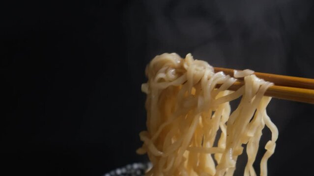 4k v&iacute;deo. Slow motion Persona cogiendo fideos chinos reci&eacute;n hechos con palillos en un fondo negro humeante. Dark food