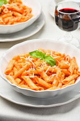 Close-up of a plate of All'Arrabbiata penne pasta and a glass of red wine on a linen tablecloth. Vertical studio shot from a high angle of view.