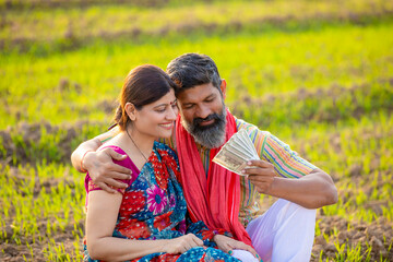 Indian farmer giving money to wife at agriculture field.