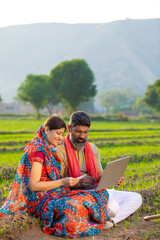 Indian farmer with wife using laptop and bank card at agriculture field.