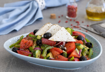Horiatiki. Homemade Greek salad consists of sliced cucumber, tomato, green bell pepper, red onion and black olives served in blue ceramic bowl topped with triangle slices of feta cheese.