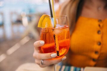 Young girl in a restaurant holding a cocktail aperol spritz in a glass