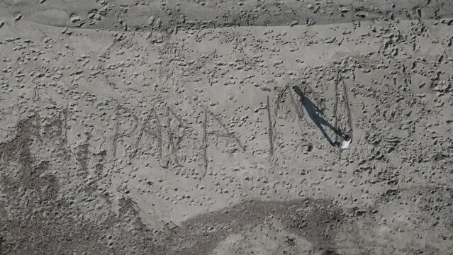 Ni&ntilde;o en la arena de la playa dibuja letras  (Formato D-log para correcci&oacute;n de color profesional)