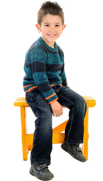 Isolated child in jeans and striped sweater smiling sitting in a yellow seat.