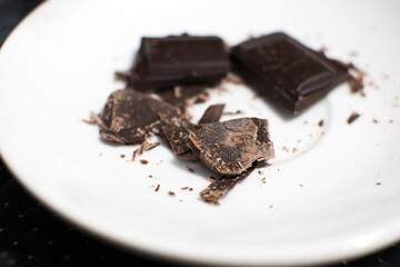 Dark crashed chocolate bar lying on the white plate. Close up photo.