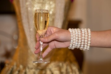 mains d'une jeune femme avec une flute de champagne avec des bracelets de perles de cultures