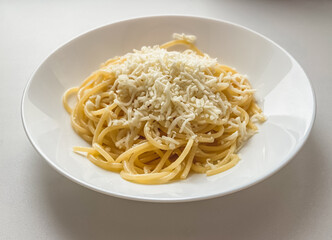 Spaghetti with cheese in a white plate on a white background.