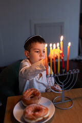 Little preschool boy lighting the Hanukkah candle on a menorah. Hanukkah lights. Jewish boy