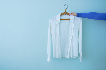 White shirt on a clothes hanger in the hand of a caucasian woman. Blue background.