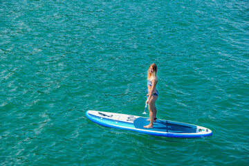 SUP Stand up paddle board. Blond girl sailing on paddle board in sea. Aerial view. Woman on summer holidays vacation lifestyle. Mtsvane Kontskhi Beach, Batumi, Georgia.
