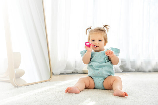 Cute baby girl playing with first toothbrush in domestic room. Copy space for advertisement
