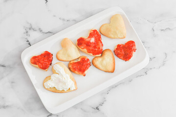Not perfect homemade heart-shaped cookies with strawberry jam and whipped cream in a white plate.
