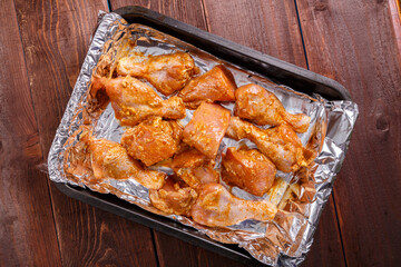 chicken drumsticks in sauce and herbs marinated on foil on a baking sheet on a wooden table.