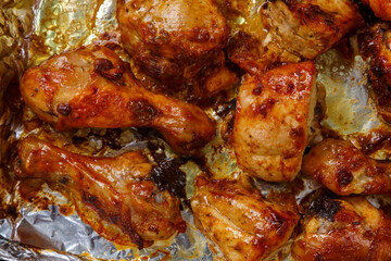 Baked chicken legs and breasts in sauce and herbs on foil close-up.