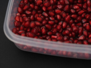 Pomegranate seeds in a plastic container on a black background