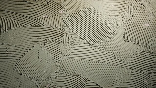 Pattern of notched trowel strokes on the gray surface of cement putty for laying ceramic tiles. Texture of glue paste with strokes and stripes. Close up of a wall surface with cement. Repair work.