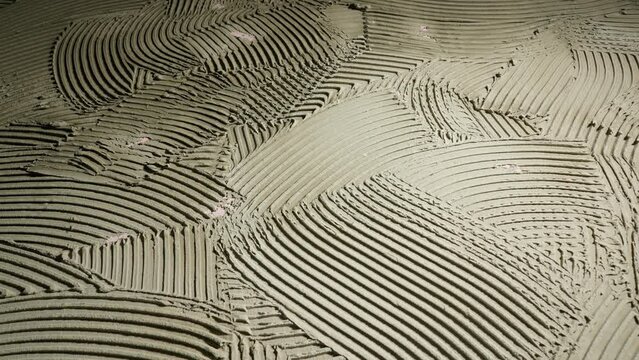 Pattern of notched trowel strokes on the gray surface of cement putty for laying ceramic tiles. Texture of glue paste with strokes and stripes. Close up of a wall surface with cement. Repair work.