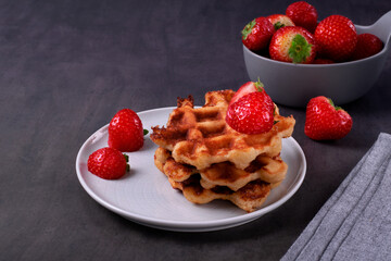 Stack of waffles with strawberry on ceramic plate on dark gray table