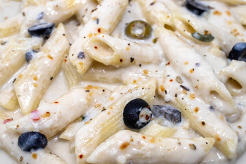 closeup view of creamy italian Alfredo penne pasta white sauce with mixed herbs, basil, parsley, onion, garlic, olives, jalapeno, cheese and garlic