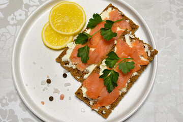 sandwiches with crisp bread, riccota and slices of salmon with parsley and lemon on white plate
