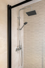 Modern shower zone with black rain head and hand held shower. Beige tiles in the bathroom.
