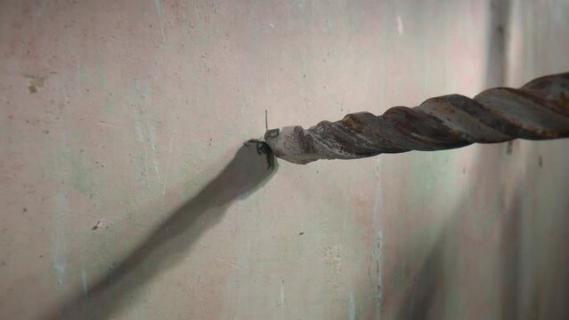 Process of drilling hole in concrete wall using electric drill or perforator. Close up of metal spiral auger drill is rotating. In process of drilling with drill, white dust from the plaster crumbles.