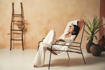 Side view of relaxed sleeping asian woman in pajama having nap on lounger in boho style room