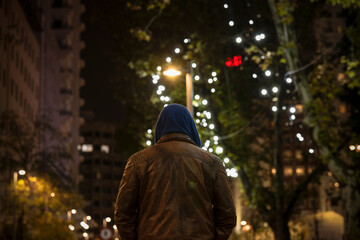 Fototapeta na wymiar Rear view of adult man on street at night with lights of Christmas