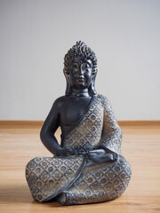 Estatua de Buda sentado en el piso de madera laminada con fondo de pared gris claro.