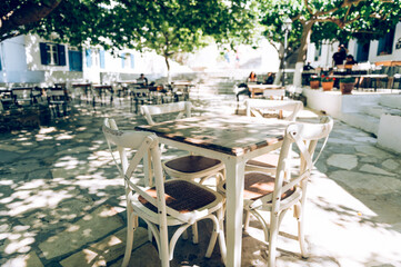 Empty cafe tables on streets of village of Tinos island with Cycladic houses on background, Cyclades, Greece