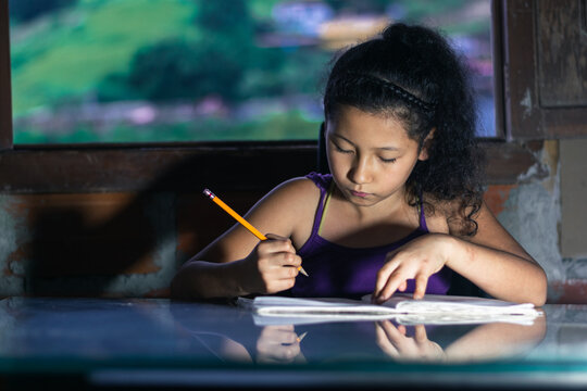 latina girl, brunette studying. little girl with a yellow pencil doing her homework, leaning on a glass table.