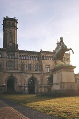 impressive historic castle like building of an university in Hanover, germany. bronze horse monument in bright morning light on forecourt. vertical orientation - obrazy, fototapety, plakaty