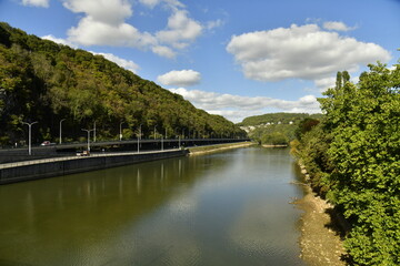 Fototapeta na wymiar La Meuse avec voie de circulation routière entre les hautes collines boisées à Lustin au sud de Namur