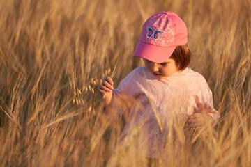 A little girl in a pink cap on a field of rye in the soft light of the setting sun.