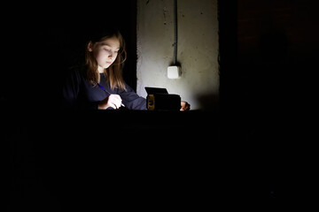 The girl learns lessons in the dark. A child does school work when there is no electricity at home.