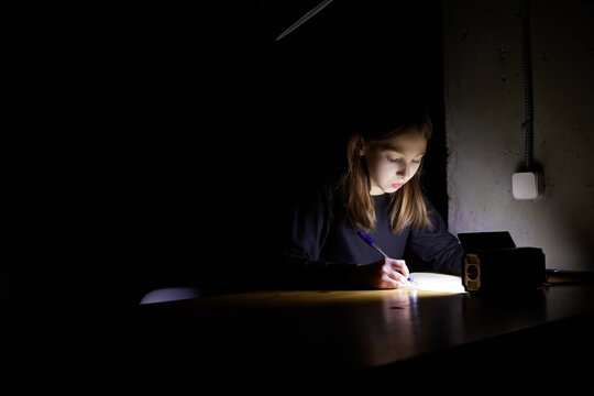 The girl learns lessons in the dark. A child does school work when there is no electricity at home.
