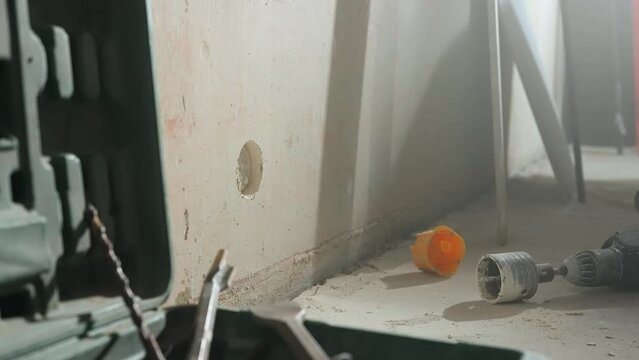 Perforator with nozzle for cutting holes for socket lying on floor next to toolbox and drills. Interior of room inside is in process of renovation. Concept of construction and repair. Close up.