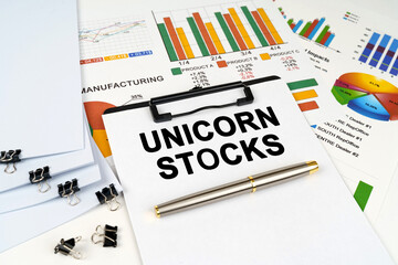 On the table among financial graphs and charts lies a tablet with the inscription - Unicorn Stocks