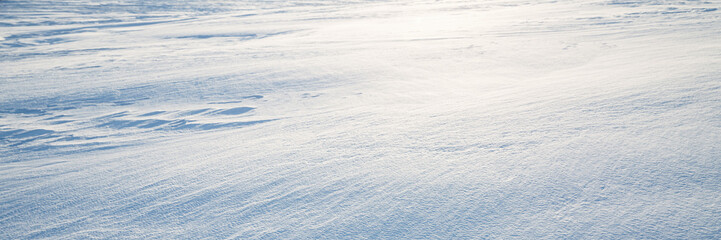 Beautiful winter background with snowy ground. Natural snow texture. Wind sculpted patterns on snow surface. Wide panoramic texture for background and design. Closeup top view with copy space.