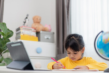 Asian schoolgirl doing her homework with digital tablet at home. Children use gadgets to study. Education and distance learning for kids. Homeschooling during quarantine. Stay at home