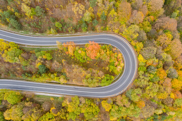 Curvy road in mountains on sunny autumn day with colorful trees, aerial top down