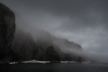Summer night arctic landscape. July. Epic view of the rocky sea coast. Cloudy and foggy rainy weather. Ice floes near the shore. Coast of the Bering Strait, Chukotka Peninsula, Far East of Russia.