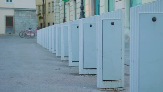 Row of parking places and charging stands for rent e-bicycles on asphalt road against bikes in street yard of Slovenian capital Ljubljana