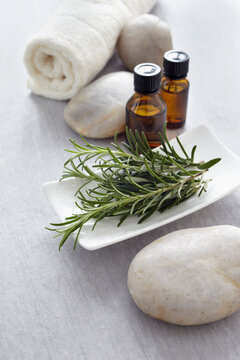 Sprig of rosemary, fresh herbs, a towel and bottles of essential oil for aromatherapy